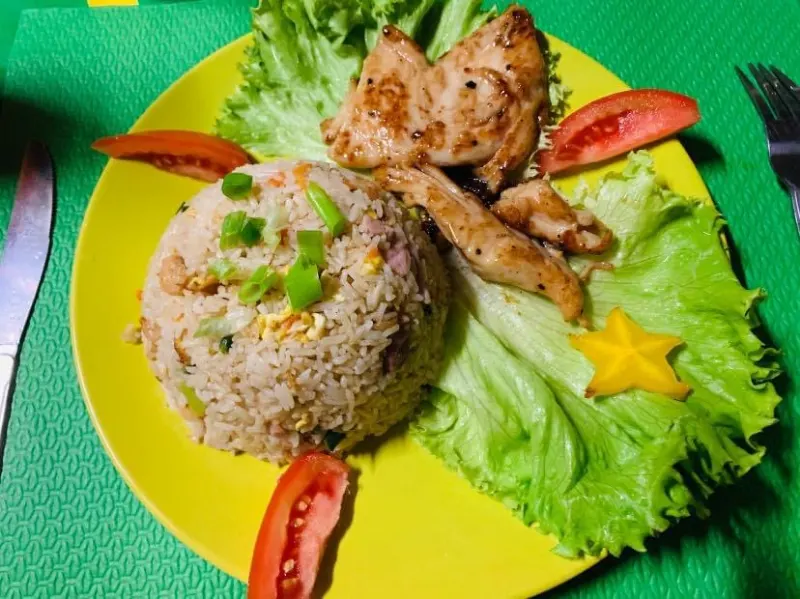 Une assiette jaune avec du riz sauté, du poulet grillé, de la salade et une carambole